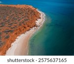 Aerial view of red cliffs and clear turquoise waters at a pristine beach in Shark Bay, Western Australia.