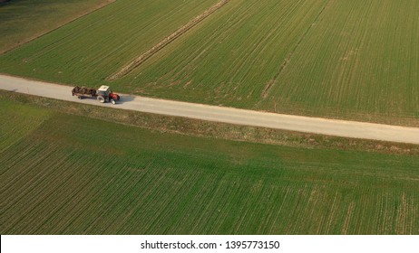 Aerial view of a red tractor and trailer carrying a load of manure on road, agriculture, fertiliying and treating soil