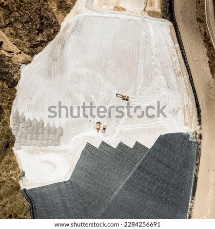 Aerial view of remediation work on a terrain with mining waste fillings, where working machinery and high-density geomembrane cover can be seen.