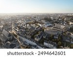 An aerial view of Rennes, France, showcasing its charming cityscape, vibrant greenery, and historic buildings bathed in the warm glow of the setting sun