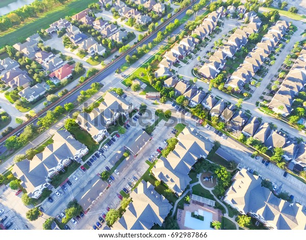 Aerial view of residential houses\
neighborhood and apartment building complex with swimming pool at\
sunset. Tightly packed homes, driveway surrounds green tree in\
Houston. Suburban housing\
development