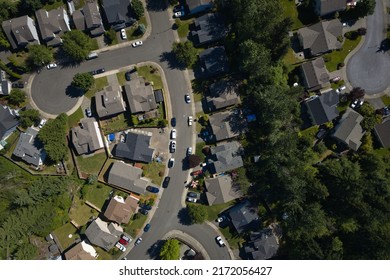 An Aerial View Of A Residential Neighborhood With Houses, Manicured Lawns, Trees, And Parked Cars Lining The Streets.