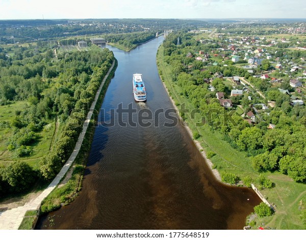 Aerial view river cruise ship sails along the river\
surrounded by beautiful green forest in summer on a sunny day.\
Cruise Ship Trip