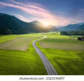 Aerial view of road in alpine mountain valley, green meadows at sunset in summer. Top drone view of country road. Colorful landscape with curved highway, hills, fields, grass, pink clouds. Slovenia - Powered by Shutterstock