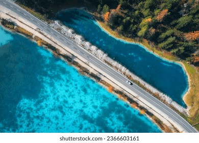 Aerial view of road, azure lakes, forest in alpine mountains in autumn sunny day. Dolomites, Italy. Travel. Top view of beautiful road, blue water, orange trees in fall. Landscape with highway. Nature