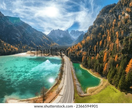 Aerial view of road, azure lakes, forest in alpine mountains in autumn sunny day. Dolomites, Italy. Travel. Top view of beautiful road, rocks, blue water, orange trees in fall. Landscape with highway