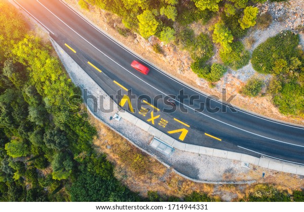 Aerial view of road in beautiful green forest at\
sunset in summer. Colorful landscape with red car on the roadway,\
trees in spring. Top view from drone of highway in Croatia. View\
from above. Travel