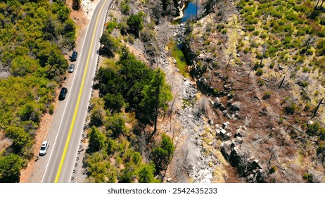 Aerial view of road beside rugged canyon landscape. An aerial view captures a winding road beside a rocky canyon with sparse greenery and a flowing stream. - Powered by Shutterstock