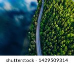 Aerial view of road between green summer forest and blue lake in Finland