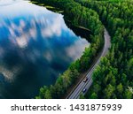 Aerial view of road between green summer forest and blue lake in Finland