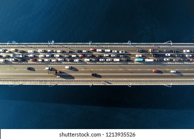 Aerial View Of Road Bridge Across River With Heavy Traffic Jam In One Direction. Rush Hour With Mash And Overloading Of Road Infrastructure. Resolving Of Car Traffic Jam.