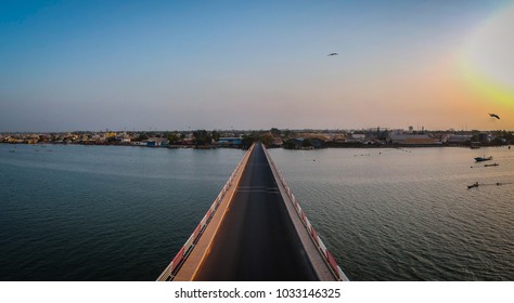 Aerial View Of The Road Bridge Over Casamance River In Ziguinchor, Senegal, Africa During A Sunset. Drone Picture Looking Towards The City Above The Driving Platform.