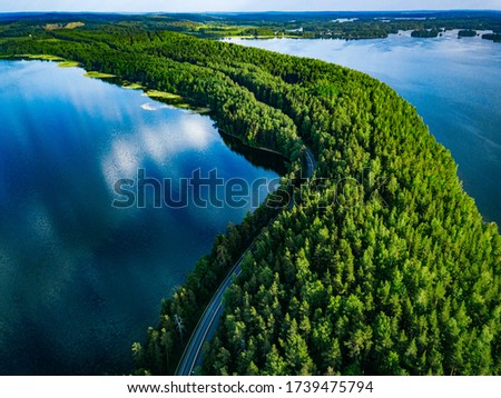 Aerial view of road with cars between green forest and blue lake water in summer Finland