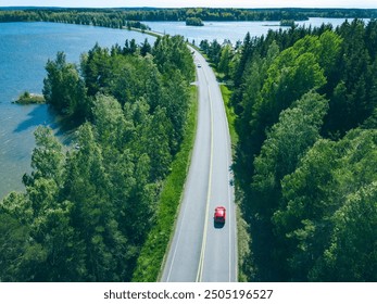 Aerial view of road with cars in green woods by blue lakes sea water in Finland