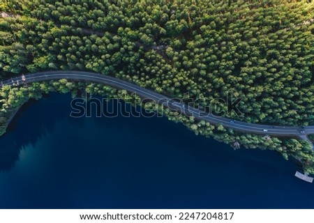 Aerial view of road with green woods by blue lakes water in summer Finland.