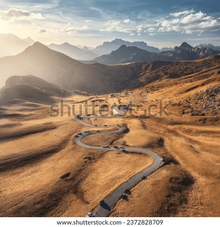 Aerial view of road in mountain valley, golden sunlight at sunset in autumn. Passo Giau, Dolomites, Italy. Top view of beautiful roadway, orange grass, alpine meadows, mountain peaks, sky in fall