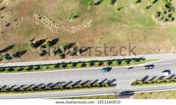Aerial view of a road with moving\
cars along the field with green bushes and brown autumn grass.\
Clip. Summer road trip concept, cars driving on a sunny\
day.