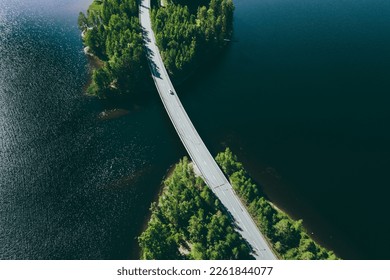 Aerial view of road over blue lake water and green woods in Finland. Beautiful summer landscape.