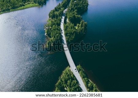 Aerial view of road over blue lake water and green woods in Finland. Beautiful summer landscape.