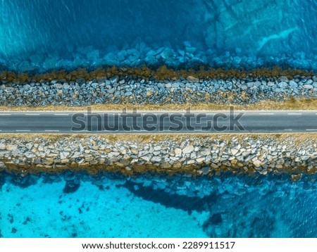 Aerial view of road, sea, stones at sunset in Lofoten Islands, Norway. Landscape with beautiful bridge, transparent blue water, rocks. Top down view from drone of highway in summer. Travel. Scenery