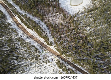 Aerial View Of The Road And Taiga Forest In Winter On A Sunny Bright Day. Abstract Landscape Of Northern Nature With Drone. Local Map