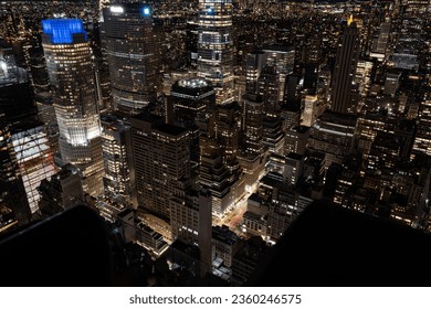 An aerial view of a Rockefeller Center in New York lit up at nightw with numerous illuminated skyscrapers