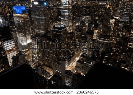An aerial view of a Rockefeller Center in New York lit up at nightw with numerous illuminated skyscrapers