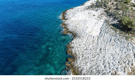 Aerial view of a rocky coastline with clear blue water and sparse vegetation. - Powered by Shutterstock