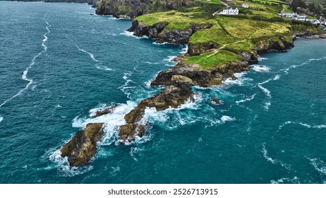 Aerial view of a rocky coastline with lush green hills and white houses on the cliffs. In Cornwall, UK. - Powered by Shutterstock