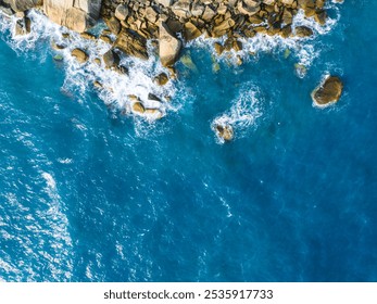 Aerial view of rocky coastline with turquoise waters and crashing waves during a sunny day - Powered by Shutterstock