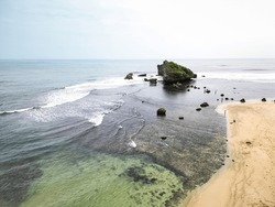 Aerial View Of A Rocky Headland With Crashing Waves During The Day. Cape With Cliffs By The Sea And Green Plants On It At Tropical Island In Ngandong Beach, Gunungkidul, Yogyakarta, Indonesia
