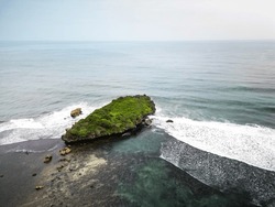 Aerial View Of A Rocky Headland With Crashing Waves During The Day. Cape With Cliffs By The Sea And Green Plants On It At Tropical Island In Ngandong Beach, Gunungkidul, Yogyakarta, Indonesia