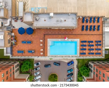 Aerial View Of Rooftop Pool With Rows Of Blue Lounging Chairs, Grill, Bar On Top Of A Luxury Downtown East Coast Residential Building In The USA