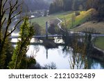 Aerial view of rope bridge near small medieval town St-Ursanne with river Doubs and defocus trees in the foreground on a winter day. Photo taken February 7th, 2022, Saint-Ursanne, Switzerland.