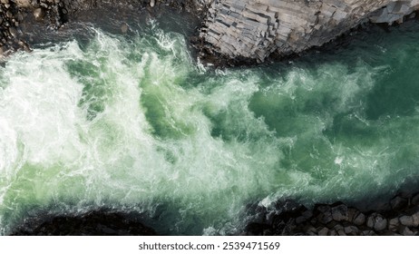 Aerial view of rugged coastal rocks surrounded by powerful, turquoise ocean waves. The churning water contrasts with the dark, jagged rocks, creating a dramatic and captivating seascape. - Powered by Shutterstock