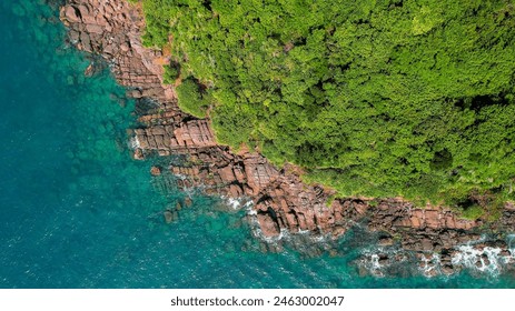 Aerial view of a rugged coastline with red rock formations and lush greenery meeting the turquoise sea, suitable for Earth Day and nature conservation topics - Powered by Shutterstock