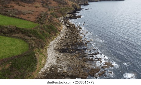 Aerial view of a rugged coastline with rocky shore and green fields meeting the ocean, showcasing natural beauty and landscape diversity. - Powered by Shutterstock