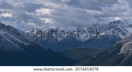 Aerial view of rugged Sundance Range in the Rocky Mountains near Canmore, Alberta, Canada with snow-capped Mount Turbulent viewed from Ha Ling Peak in autumn with cloudy sky.