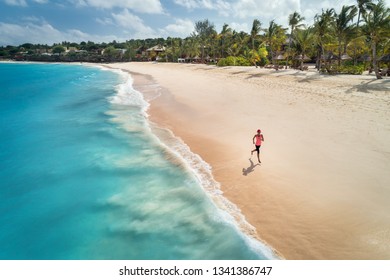 Aerial View Of The Running Young Woman On The White Sandy Beach Near Sea With Waves At Sunrise. Summer Holiday. Top View Of Sporty Slim Girl, Clear Azure Water. Indian Ocean. Lifestyle And Sport