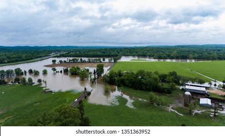 Aerial View Of Rural Farm Affected By Spring Flooding Featuring Farm House, Silo On Dry Ground, Livestock, Green Fields, Brown Flood Water, Covered Roads