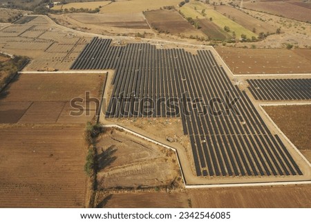 An aerial view of a rural landscape featuring a large solar array and the backdrop of a mountain range
