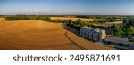 Aerial view of rural landscape with golden wheat fields, silos, farm buildings, barn and wind turbines, highlighting modern agriculture and renewable energy.