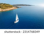 Aerial view of sailboat on blue sea at sunset in summer. Travel in Sardinia, Italy. Tropical seascape with sailing boat, sea bay, mountain, green trees, ocean, sky. Top drone view yacht. Yachting