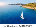 Aerial view of sailboat on blue sea at sunset in summer. Travel in Sardinia, Italy. Tropical seascape with sailing boat, sea bay, mountain, green trees, ocean, sky. Top drone view yacht. Yachting