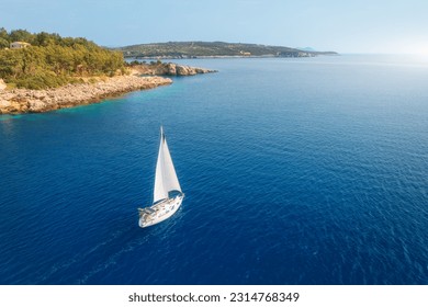 Aerial view of sailboat on blue sea at sunset in summer. Travel in Sardinia, Italy. Tropical seascape with sailing boat, sea bay, mountain, green trees, ocean, sky. Top drone view yacht. Yachting - Shutterstock ID 2314768349