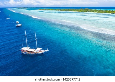 Aerial view of sailing boat anchoring on coral reef. Drone view, water sport theme. Luxury cruise and marine travel background. Beautiful nature scenery, sea ocean water concept. Maldives aerial