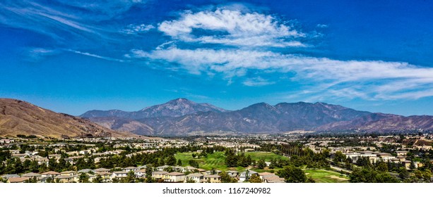 Aerial view of San Gorgonio Mountain in the San Bernardino Mountains above Yucaipa Valley, California with blue sky, white clouds, purple mountains and green grss