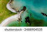An aerial view of a sandy beach curving into turquoise waters, framed by lush green grass and rocky inlets. top view at beach of Kolbeinsanden Beach, Lofoten