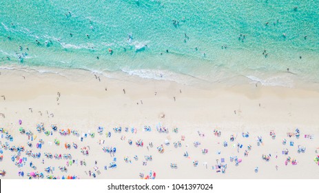 Aerial view of sandy beach with tourists swimming in beautiful clear sea water.