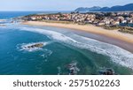 An aerial view of sandy Ris Beach, Atlantic Ocean waves, islets, Noja village, and distant mountains. Noja, Cantabria, Spain.